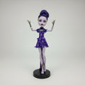 Monster High doll with purple hair and dress on a black background