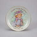 Decorative plate with a girl in a hat and dress, featuring 'Cherished Moments Last Forever' text.