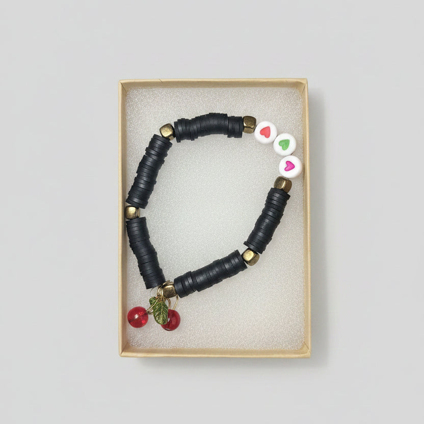 Black beaded bracelet with cherry charms in a display box on a black background