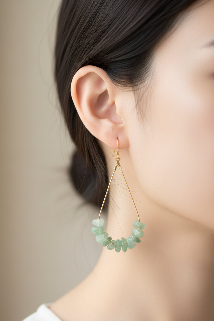 Pair of green stone earrings on a clear card with a wooden surface underneath