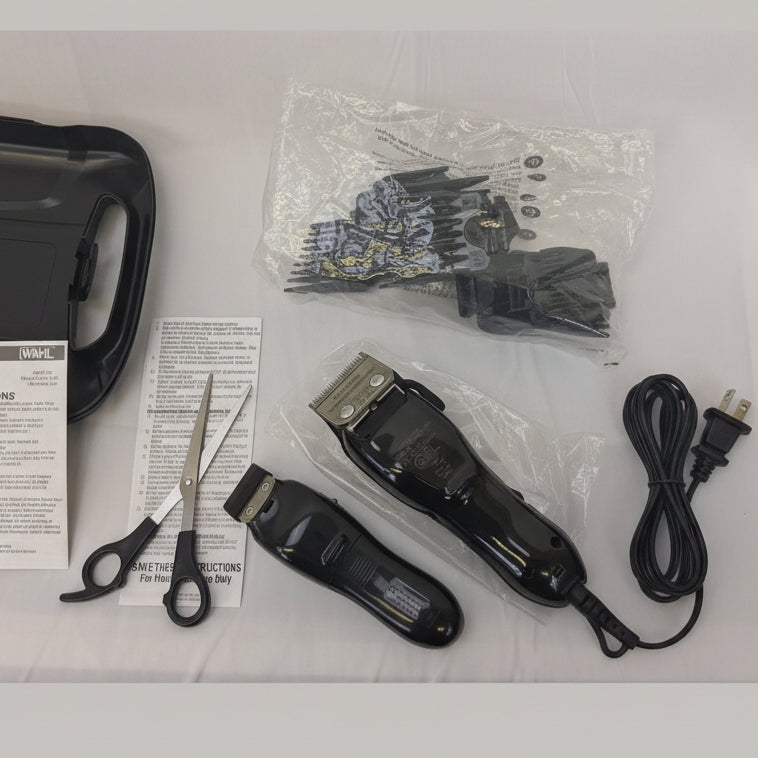Black cordless electric hair clippers shown with accessories on a white cloth-covered surface, including a carrying case, instruction booklet, scissors, a guard blade set in a clear plastic bag, and the power cord.